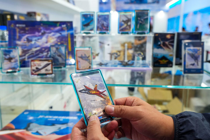 9月19日至23日，2025年长春航空展在长春国际航空博览城举办，吸引诸多参观者观展。图为一位参观者在展会现场选购航空文创产品卡游致胜空天中国战机卡牌。新华社记者 许畅 摄